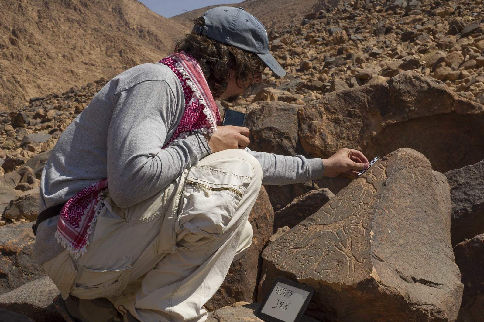 Glenn Corbett places a scale on a stone carved with several Hismaic inscriptions, one of which signs a scene of an ibex hunt. Photo by Michael Fergusson.